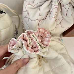 Close-up of quilted cream drawstring bag with rabbit embroidery and pink checkered lining