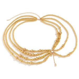 Detail of layered gold body chain with metal beads and tassel pendant on white backdrop