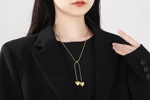 Close-up of a gold snake chain necklace with heart pendants worn over a black blazer