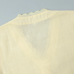 Détail de l'encolure en V festonnée et tissu texturé en coton-lin sur un haut beige