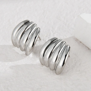 Minimalist silver wavy textured stud earrings on a white textured stone background