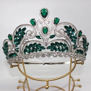 Detail of silver bridal crown featuring green emerald gems and leaf patterns on a stand