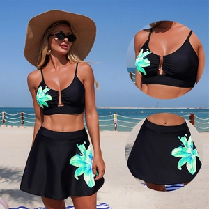 Two-piece black bikini set with blue floral print and metal ring cutout on a beach background