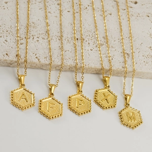 Golden hexagon titanium steel initial necklaces with engraved letters on stone background