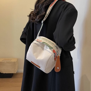 White canvas crossbody bag with colorful strap and leather zipper pull on model