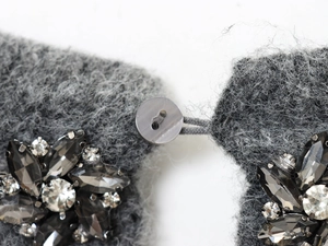 Dettaglio di un maglione grigio scuro con decorazioni in cristallo e un bottone rotondo