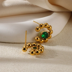 Macro shot of gold-plated beaded hoop earrings with a sparkling green zircon center