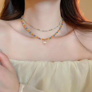 Détail d'un collier double rang en perles colorées avec un pendentif cœur transparent