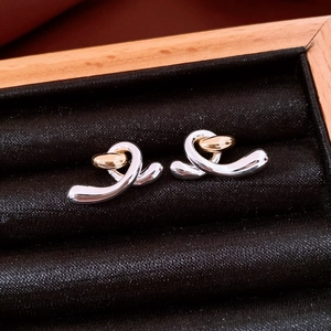 Nahaufnahme von zweifarbigen Knotenohrringen in einer Samtbox mit edlem Metallglanz