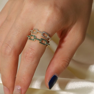 Detail of 18k gold plated chain rings with white and green gemstones on a model hand