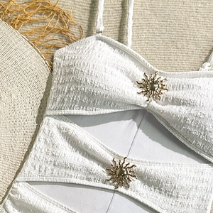 Close-up of white seersucker swimsuit fabric with gold sun-shaped metal ornaments