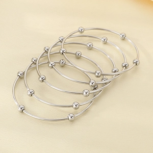 Detail of five stackable silver bangles with minimalist round bead charms on textured surface