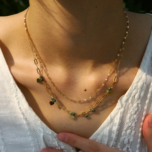 Detail of layered gold heart necklace with green beads worn on lace garment