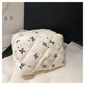 Close-up of white quilted cosmetic bag with black bow patterns and a 3D ribbon detail