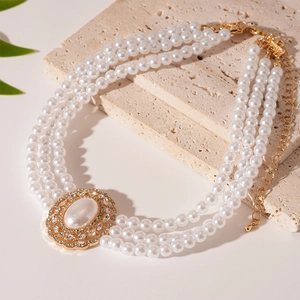 Three-strand faux pearl necklace with ornate rhinestone oval pendant on stone background