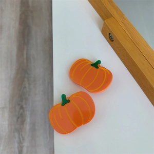 Detail view of two orange acetate pumpkin hair clips with smooth texture and green stems