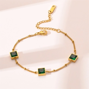 Detailed close-up of gold chain bracelet with three square emerald green stones and clasp