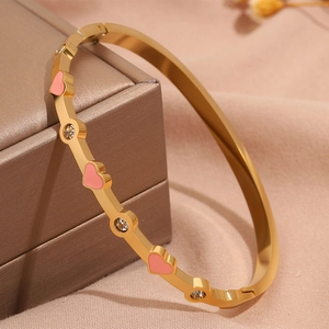 Dettaglio del bracciale in titanio placcato oro con cuori in smalto rosa e cristalli