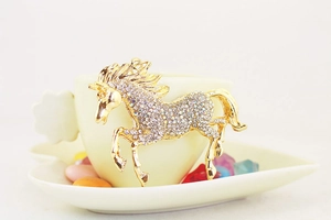 Macro shot of gold horse keychain with sparkling rhinestones on a decorative ceramic saucer