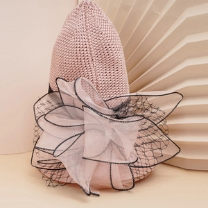 Detail of light pink knitted hat featuring large organza bow and black lace trim