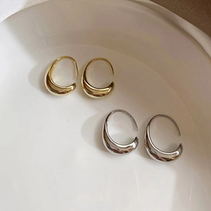 Close-up of polished gold and silver water drop hoop earrings in a white ceramic dish