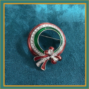 Close-up of a Christmas wreath brooch with red and green enamel, rhinestones and a bow