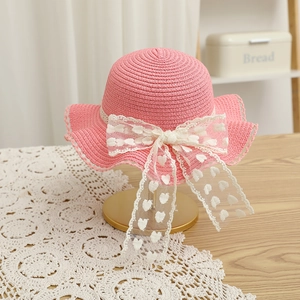 Détail d'un chapeau de paille rose avec nœud en dentelle et motifs de cœurs sur support
