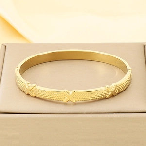 Detail of gold wave knot bangle featuring X-shaped accents and mesh texture on metal