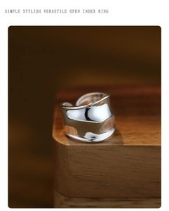 Close-up of a wide silver open index ring with irregular twisted texture on a wooden block
