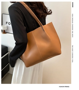 Brown leather tote bag worn by a model in a minimalist modern interior setting