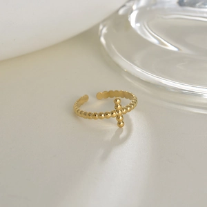 Detail of 14K gold plated beaded open ring with a small cross motif on a white surface