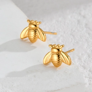 Minimalist 18K gold plated bee stud earrings on white stone texture background