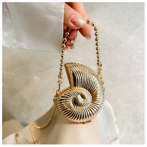Detail of shell-shaped golden evening clutch with spiral texture and beaded handle chain