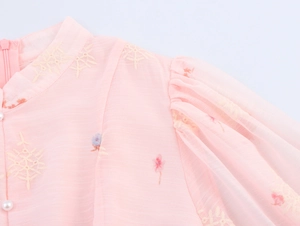 Detail van roze chiffon jurk met bloemenborduursels en elegante parelmoeren knopen