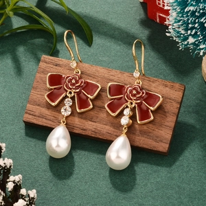 Close-up of pearl earrings with red enamel bows, roses, and sparkling crystal details