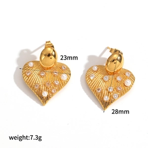 Detailed view of gold heart earrings with pearl inlay and textured leaf patterns