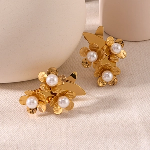 Golden hammer-textured metal flower earrings with white pearl accents on beige linen background
