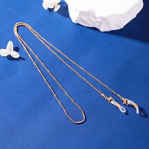 Golden beaded metal eyewear chain with silicone loops on a textured blue background