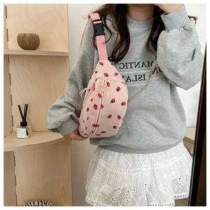 Pink corduroy waist bag with strawberry pattern shown as a crossbody on a model
