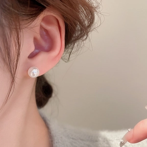 Close-up of a classic white round pearl stud earring worn by a model on the ear
