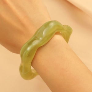 Detail of a wavy translucent green resin cuff bracelet shown on a model's wrist