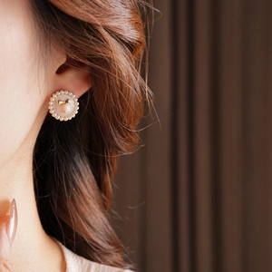 Macro shot of retro pearl stud earrings with pink bead and golden bow detail on model