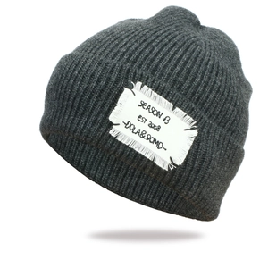 Dark grey chunky knit beanie with a vintage white patch label shown at a 45-degree angle
