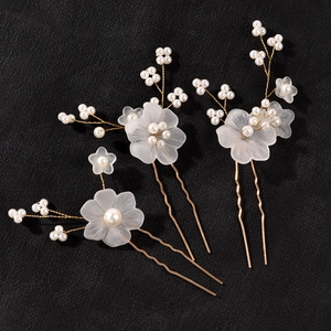 Three gold U-shaped hair pins with matte white flowers and pearls on black background