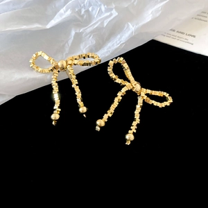 Gros plan de boucles d'oreilles nœud dorées texturées avec de longs pendentifs perlés