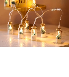 Close-up of glass wishing bottle LED lights with mini Christmas tree and snow detail