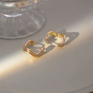 Detailed view of wavy gold irregular geometric earrings resting on a smooth surface