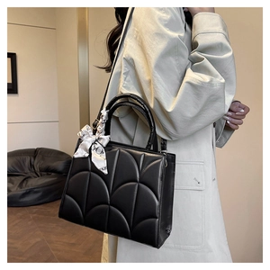 Close-up of black quilted shoulder bag featuring a stylish silk scarf handle detail