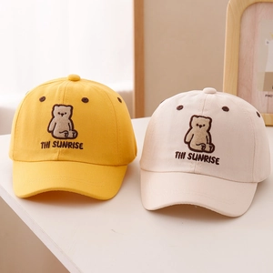 Detail of yellow and beige cotton baseball caps featuring cute bear embroidery for kids