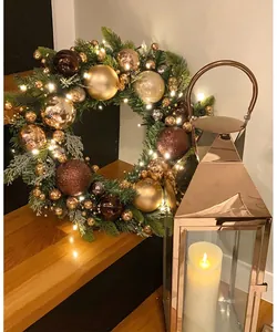 Close-up of a festive Christmas wreath with gold ornaments and a warm LED lantern on wood